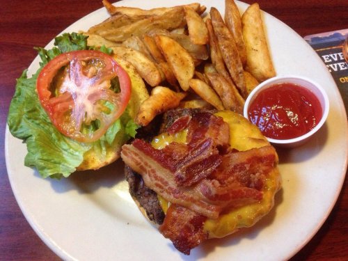 A plate featuring a cheeseburger with bacon, lettuce, and tomato, served with crispy fries and a side of ketchup.