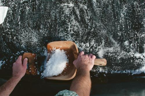 A person scoops snow with a wooden shovel from a dark surface, creating a snowy scene.
