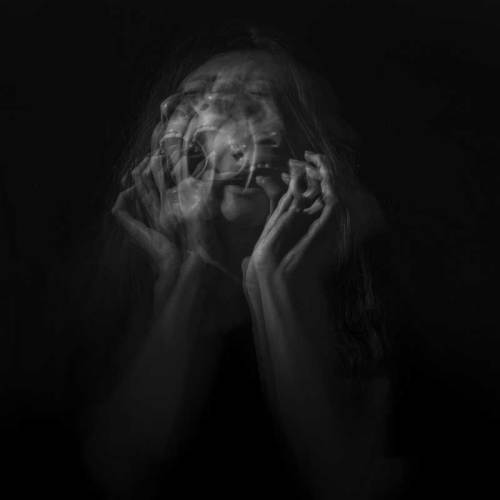 A blurred, black-and-white image of a person with multiple overlapping hand gestures, conveying a sense of distress.