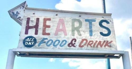 Sign for "Hearts All Day Food & Drink" with colorful, weathered letters against a blue sky.