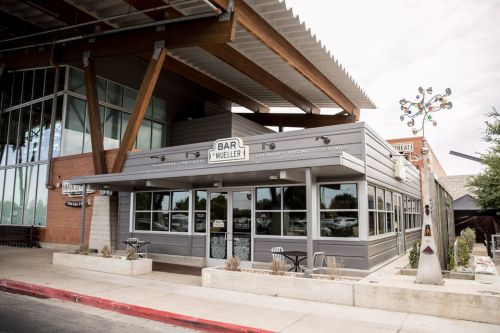 Exterior view of Bar Mueller, a modern restaurant with large windows and a unique sign, surrounded by a paved area.