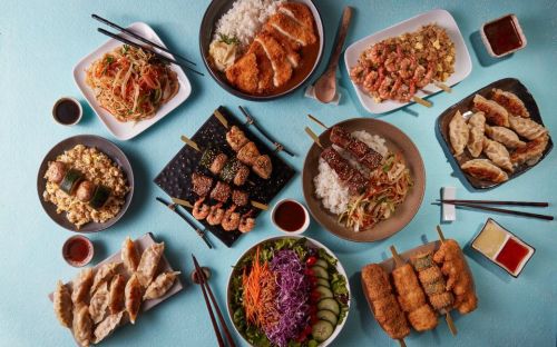 A vibrant spread of various Asian dishes, including fried rice, dumplings, skewers, and noodles, arranged on colorful plates.