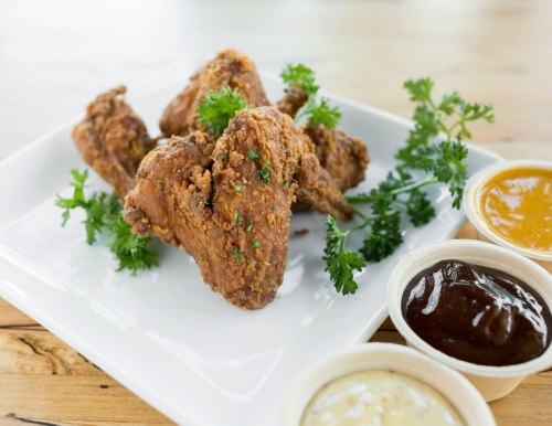 A plate of crispy fried chicken wings garnished with parsley, accompanied by three dipping sauces.