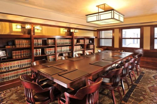 A spacious conference room with a large wooden table, leather chairs, and bookshelves filled with legal books.