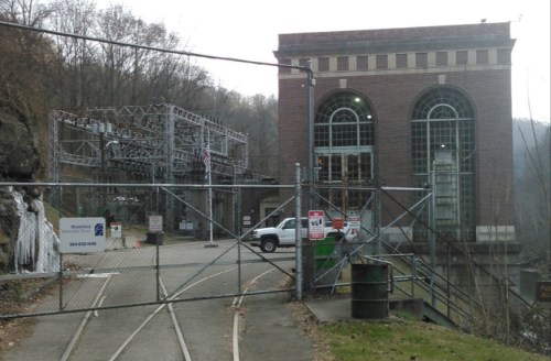 A brick building with large windows, surrounded by a fence, near power lines and a small waterfall.