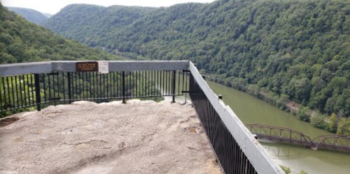 View from a lookout point overlooking a river winding through lush green mountains. A sign is visible nearby.