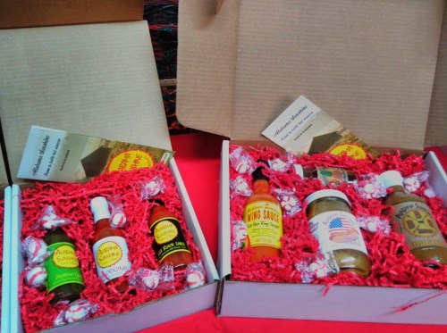 Two gift boxes filled with various sauces and seasonings, surrounded by red shredded paper and decorative items.