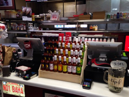 A counter at a restaurant featuring a variety of hot sauces, cash registers, and a tip jar.