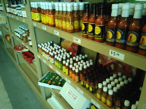 A display of various hot sauces on shelves, featuring colorful bottles and price tags.