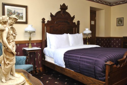 A cozy bedroom featuring a wooden bed, elegant lamps, and decorative wall art, with a statue in the foreground.