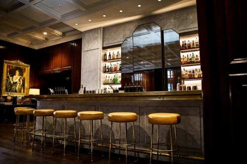 A stylish bar with a marble counter, gold stools, and shelves lined with bottles, set in an elegant room.