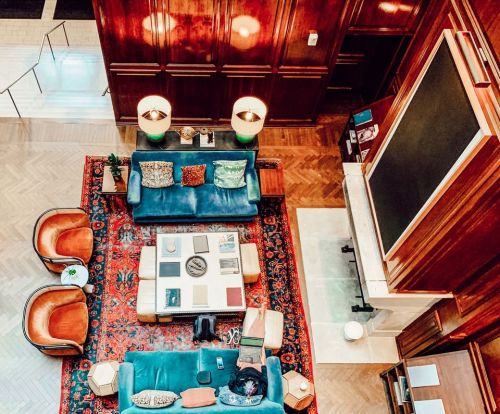 A cozy lounge with blue sofas, orange chairs, a large rug, and a fireplace, viewed from above.