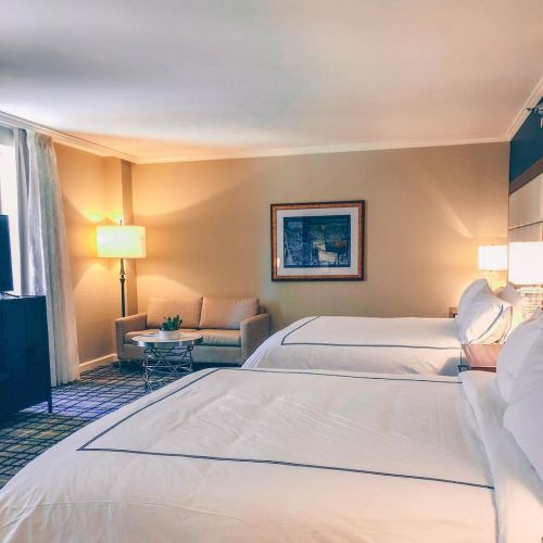 A cozy hotel room featuring two beds, a seating area, and warm lighting.