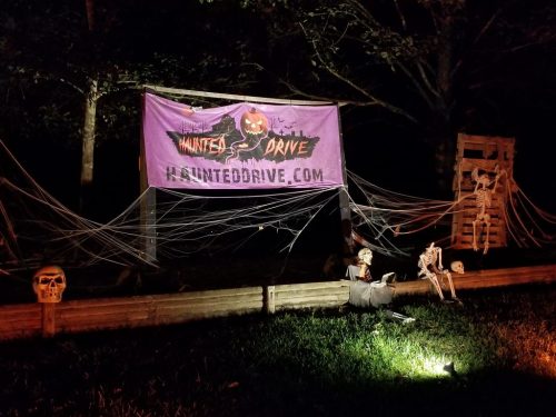 A spooky outdoor scene featuring a haunted drive banner, skeletons, and cobwebs in a dimly lit setting.
