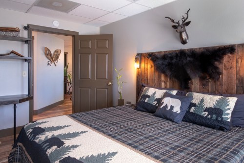 Cozy bedroom with a wooden headboard, plaid bedding, and rustic decor, featuring a deer mount and wall art.