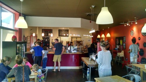 A busy café interior with customers at the counter and seated at tables, featuring bright lighting and colorful decor.