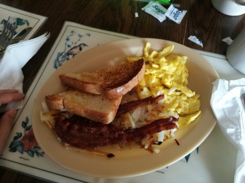A plate with scrambled eggs, crispy bacon, hash browns, and two slices of toasted bread.