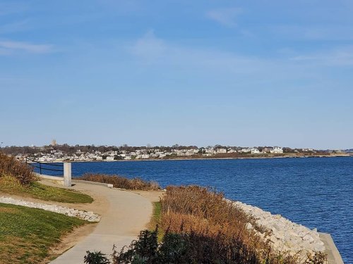 A scenic view of a coastal path along the water, with houses in the distance and clear blue skies.