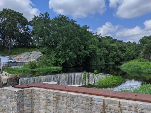 A serene landscape featuring a waterfall, lush greenery, and a calm river under a partly cloudy sky.
