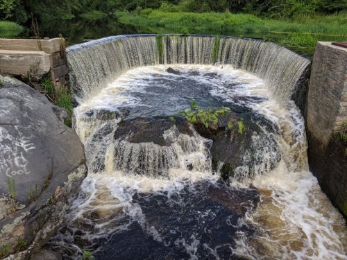 A waterfall cascading over a stone dam, surrounded by lush greenery and flowing water.
