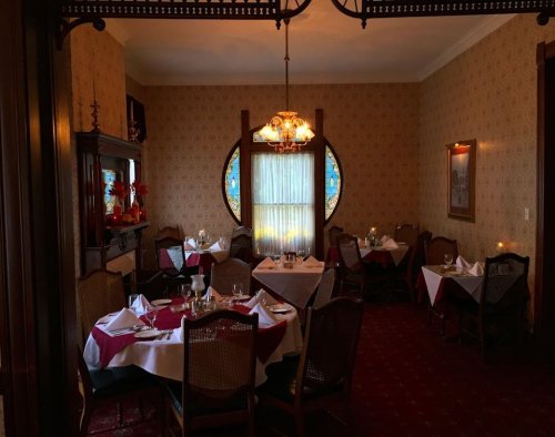 Cozy restaurant interior with elegant tables, stained glass window, and warm lighting, creating an inviting atmosphere.
