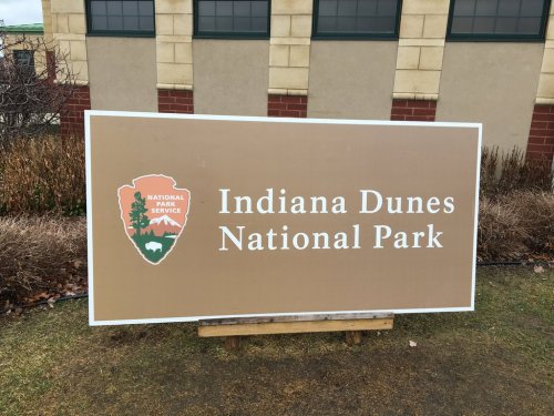 Sign for Indiana Dunes National Park, featuring the National Park Service logo and surrounded by greenery.