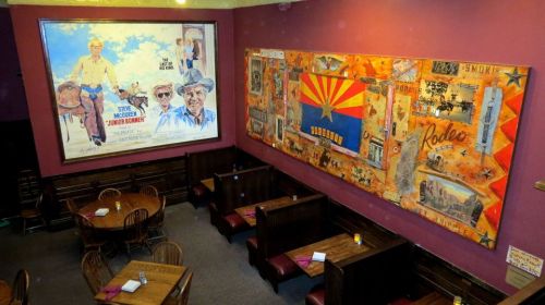 Interior of a restaurant featuring vintage Western-themed artwork and wooden tables.