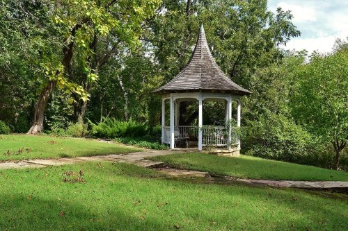 A charming gazebo with a pointed roof surrounded by lush greenery and a winding stone path.