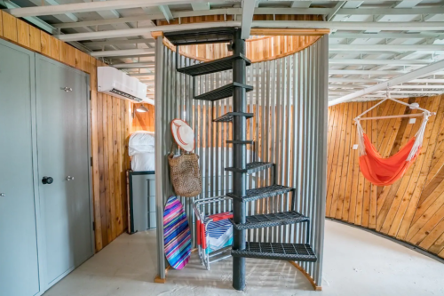A spiral staircase in a cozy, wooden interior with a hammock, storage, and beach gear.