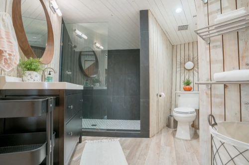 Modern bathroom featuring a glass shower, dark cabinetry, wooden accents, and stylish decor.