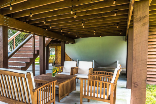 Cozy outdoor seating area with wooden furniture, a table, and string lights under a wooden deck.