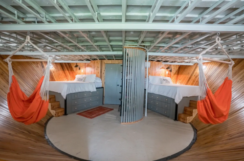 Cozy circular room with two beds, orange hammocks, wooden walls, and a spiral divider.