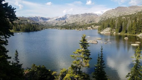 A serene lake surrounded by mountains and lush green trees under a clear blue sky.