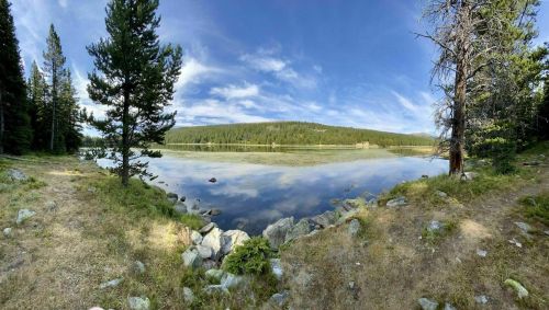 A serene lake surrounded by trees and rocky shorelines under a clear blue sky with wispy clouds.