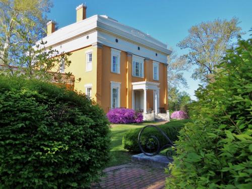 A bright yellow historic mansion surrounded by lush greenery and blooming purple flowers under a clear blue sky.