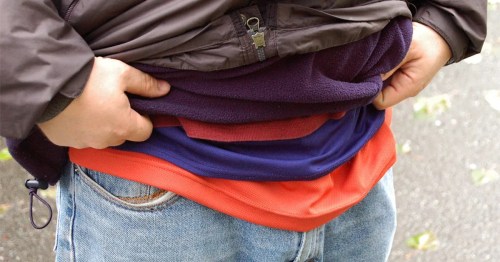 A person wearing multiple layers of clothing, including a jacket and several shirts, with hands adjusting the layers.