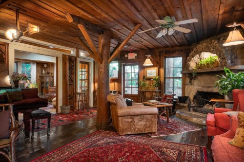 Cozy living room with wooden beams, a stone fireplace, and warm lighting, featuring plush seating and vibrant rugs.