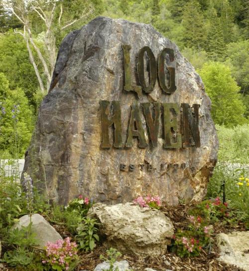 A large rock sign reading "LOG HAVEN EST. 1990" surrounded by greenery and colorful flowers.