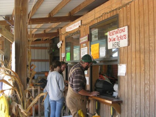 A rustic ticket booth with wooden walls, where two people are purchasing tickets amidst autumn decorations.