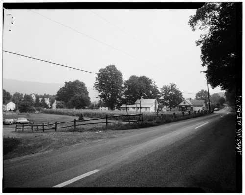 A rural scene featuring a road, trees, and several houses in a quiet landscape, captured in black and white.