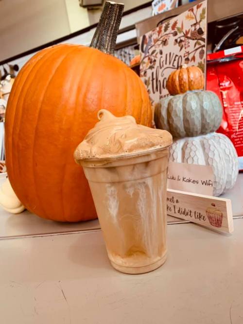 A pumpkin and decorative gourds beside a cup of frothy coffee or dessert, with a sign that reads "not a cake I didn't like."