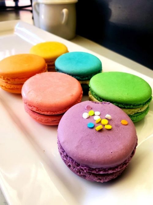 A colorful assortment of macarons in orange, yellow, pink, blue, green, and purple arranged on a white plate.