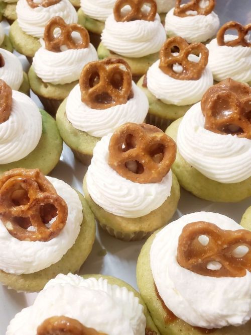Close-up of cupcakes topped with whipped cream and mini pretzels, arranged neatly on a tray.