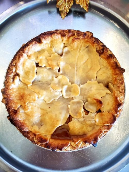 A golden-brown pie topped with decorative leaf-shaped crust pieces, resting on a silver tray.