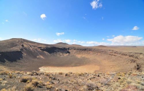 A vast volcanic crater surrounded by rocky terrain under a clear blue sky with scattered clouds.