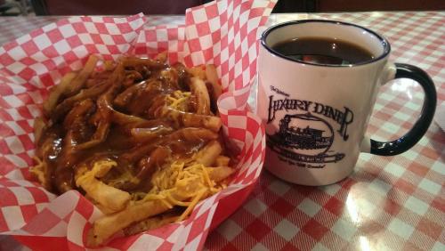 A basket of loaded fries topped with cheese and gravy next to a mug of coffee on a checkered tablecloth.