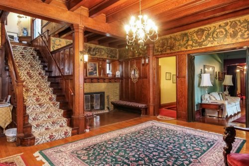A spacious, vintage foyer with a staircase, ornate woodwork, a chandelier, and a large area rug.