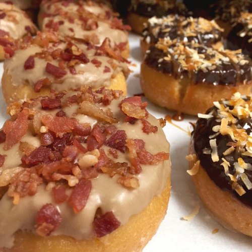 A close-up of two types of donuts: one topped with maple icing and bacon bits, the other with chocolate and coconut.