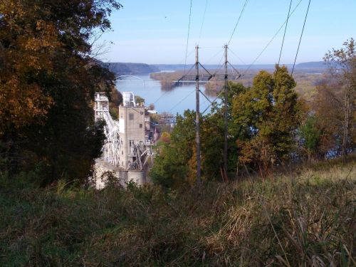 A view of a river with power lines, surrounded by trees and hills, showcasing a serene landscape in autumn.