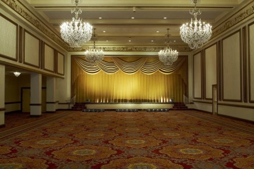 Elegant event space with a golden curtain backdrop, chandeliers, and ornate carpet. Ideal for performances or gatherings.